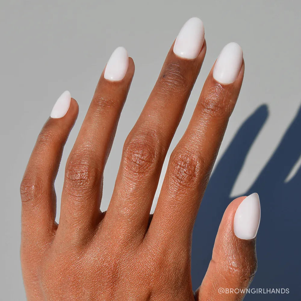 A hand with medium brown skin and short oval nails wears glamnetic's Clean Girl milky manicure, displayed against a neutral background with visible shadow.
